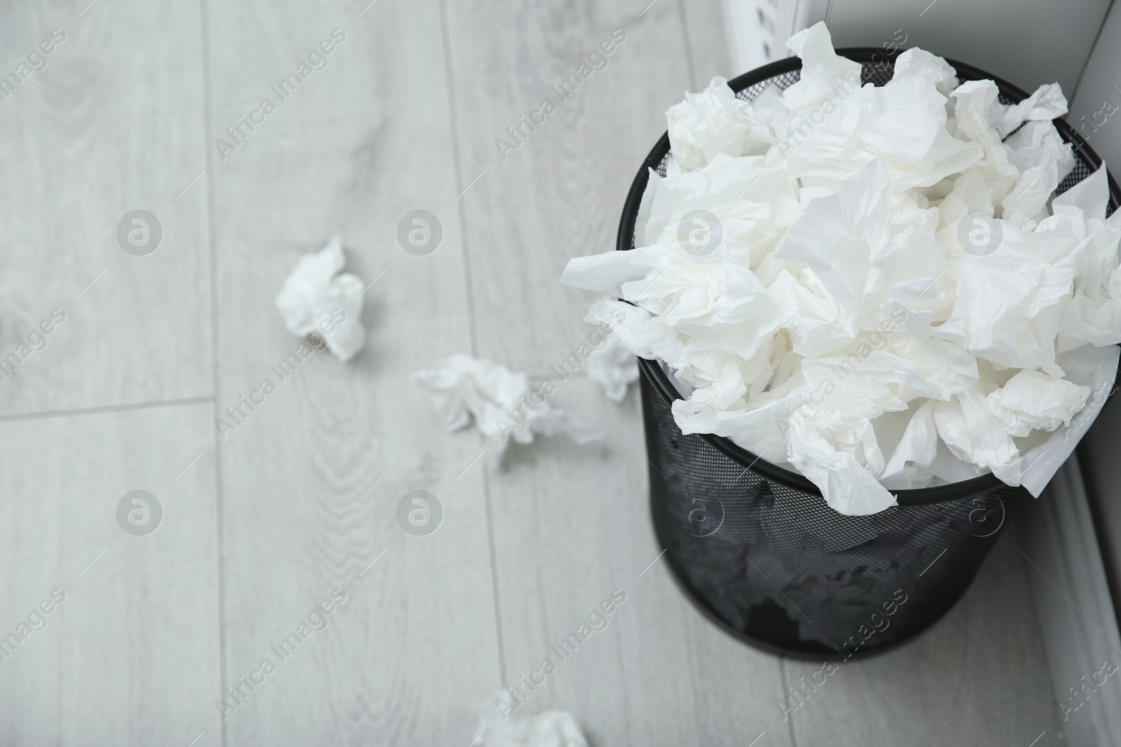 Photo of Used paper tissues in trash can on wooden floor. Space for text