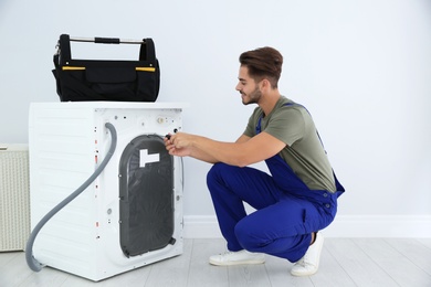 Photo of Young handyman fixing washing machine at home. Laundry day