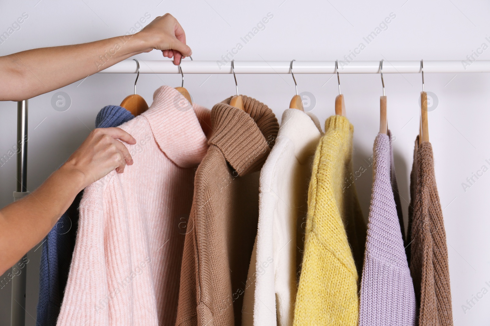 Photo of Woman choosing sweater on rack against white background, closeup