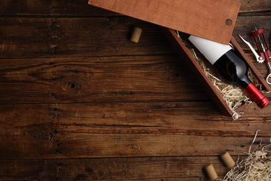 Photo of Box with wine bottle, corkscrew and corks on wooden table, flat lay. Space for text