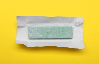 Photo of Unwrapped stick of chewing gum on yellow background, top view