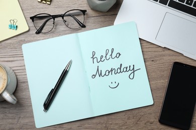 Photo of Message Hello Monday written in notebook, office stationery and smartphone on wooden desk, flat lay