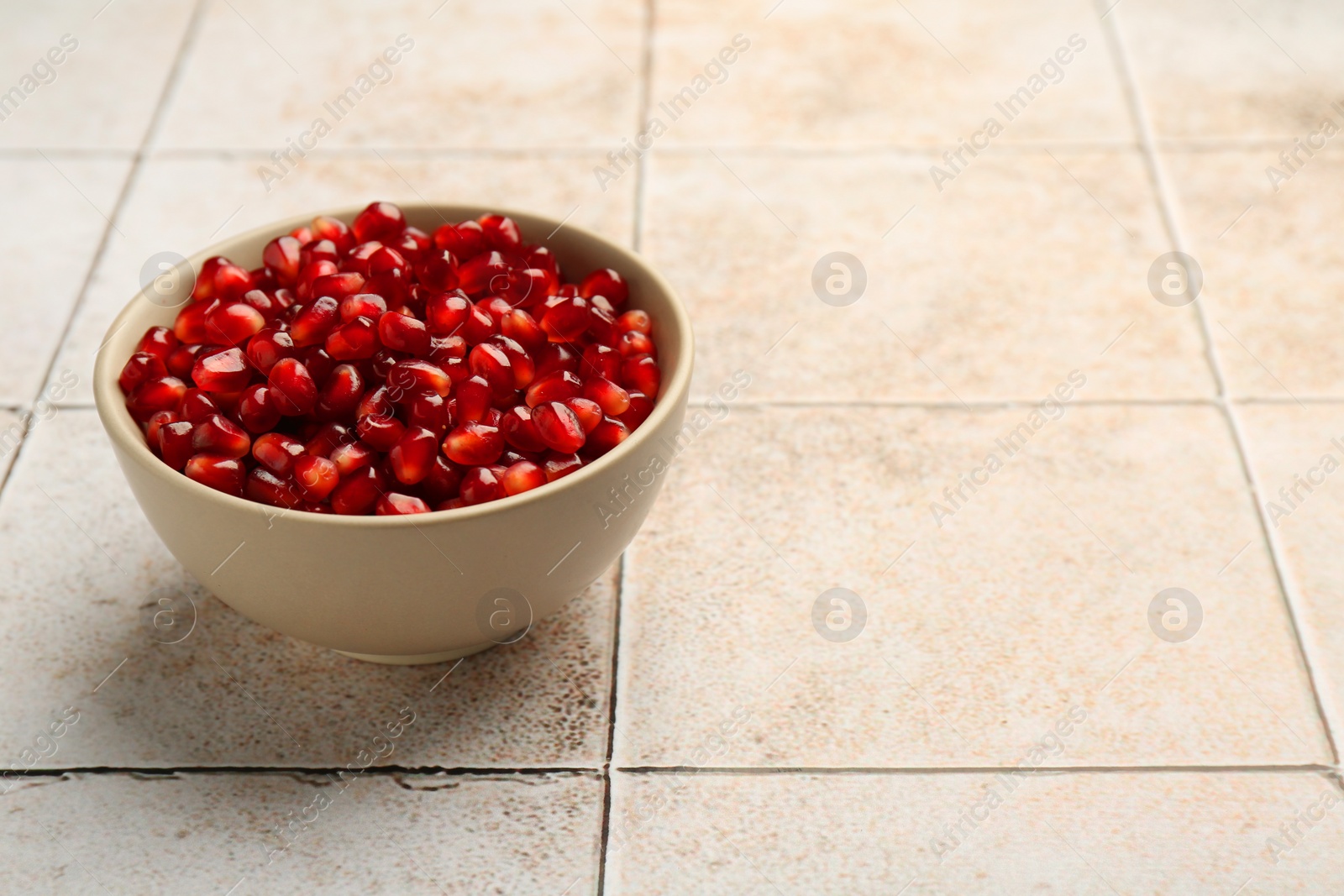 Photo of Tasty ripe pomegranate grains on tiled table. Space for text