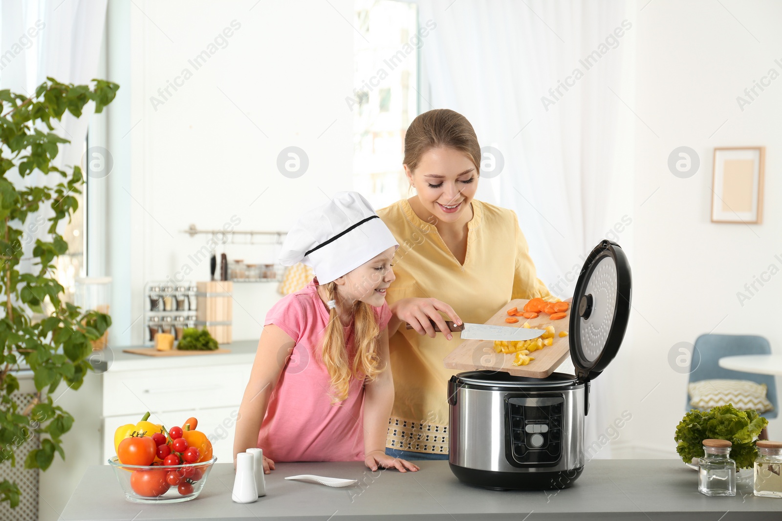 Photo of Mother and daughter preparing food with modern multi cooker in kitchen