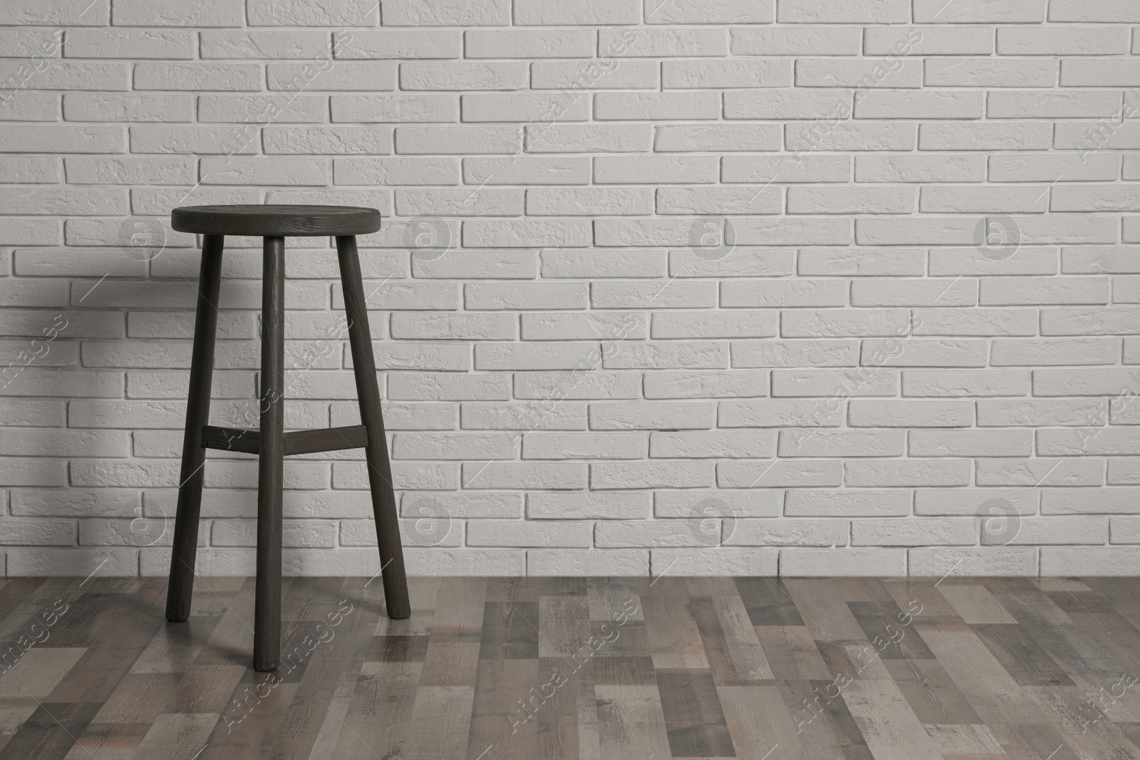 Photo of Stylish wooden stool near white brick wall indoors. Space for text