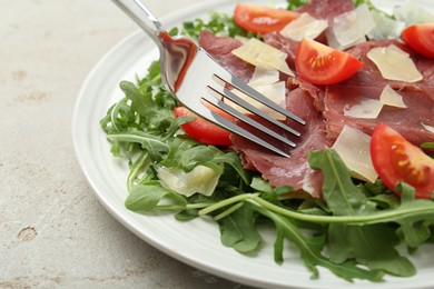 Photo of Eating delicious bresaola salad at light grey textured table, closeup
