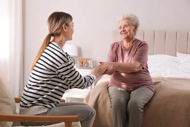 Photo of Young caregiver talking to senior woman in bedroom. Home care service