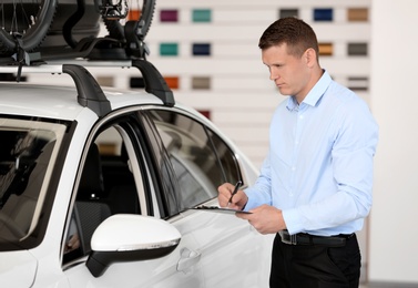 Young salesman with clipboard in car dealership
