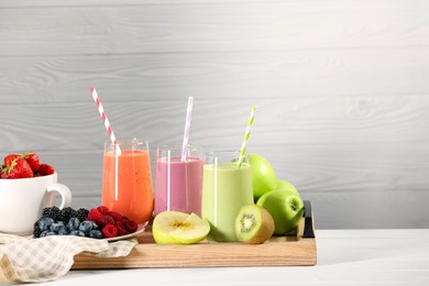 Photo of Glasses of different tasty smoothies and fresh ingredients on white wooden table. Space for text
