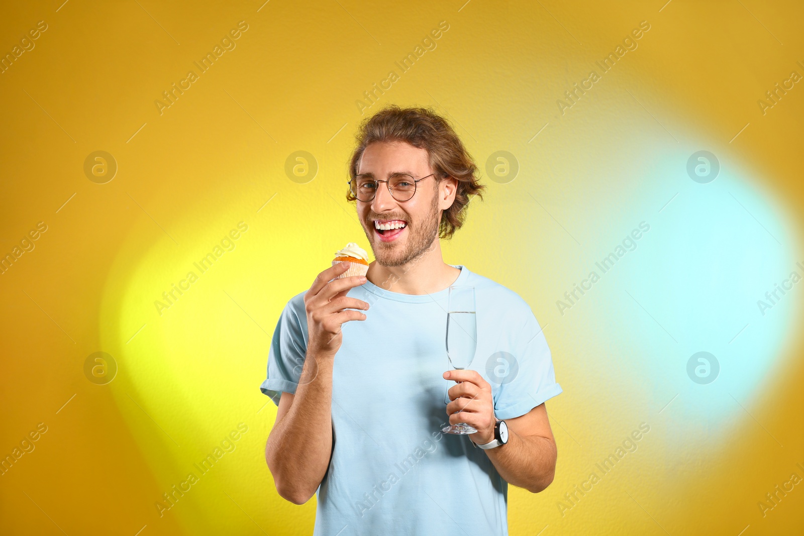 Photo of Portrait of happy man with champagne in glass and tasty cupcake on color background