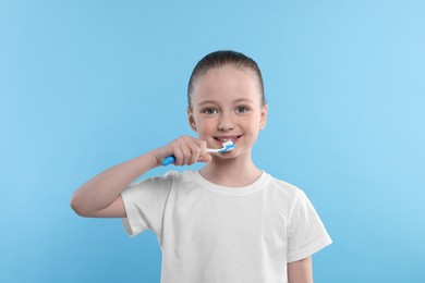 Photo of Happy girl brushing her teeth with toothbrush on light blue background