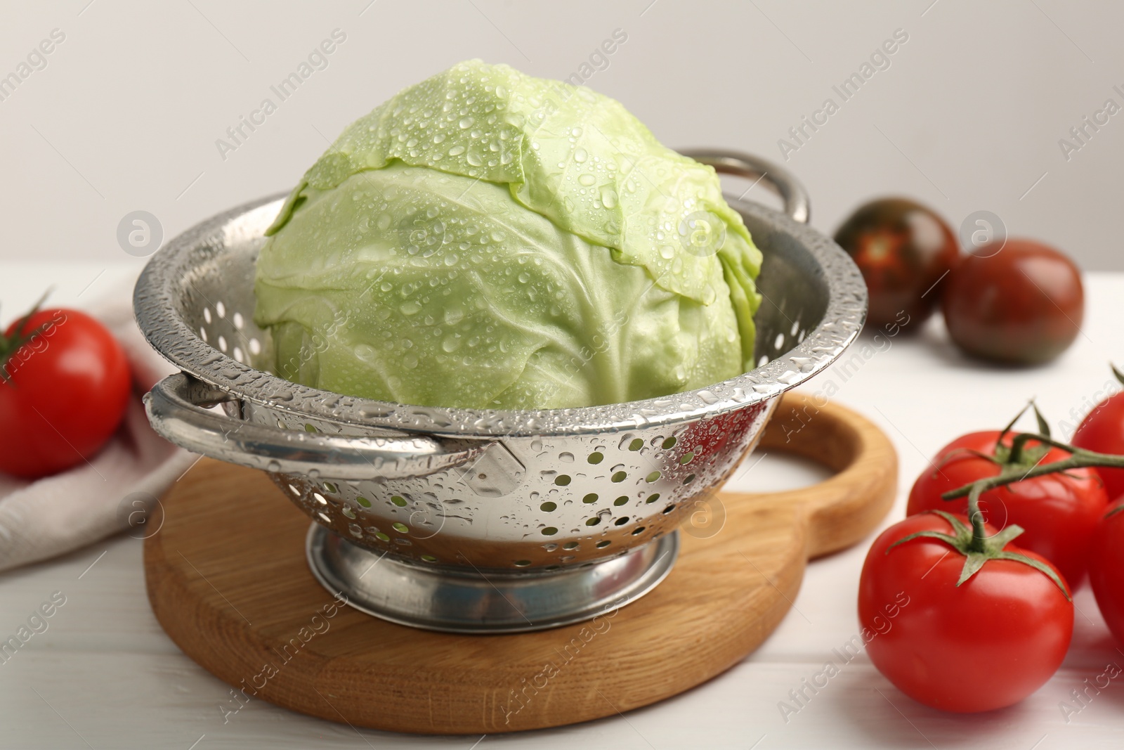 Photo of Wet cabbage in colander and tomatoes on white wooden table, closeup