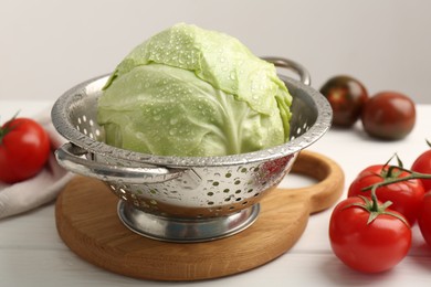 Photo of Wet cabbage in colander and tomatoes on white wooden table, closeup