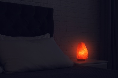 Photo of Himalayan salt lamp glowing on bedside table in dark room