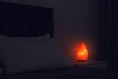 Himalayan salt lamp glowing on bedside table in dark room