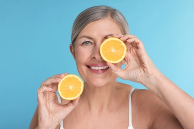 Beautiful woman with halves of orange rich in vitamin C on light blue background