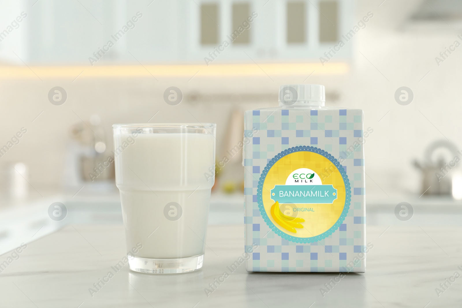 Image of Carton box and glass of banana milk on table in kitchen. Vegan product