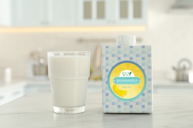 Carton box and glass of banana milk on table in kitchen. Vegan product