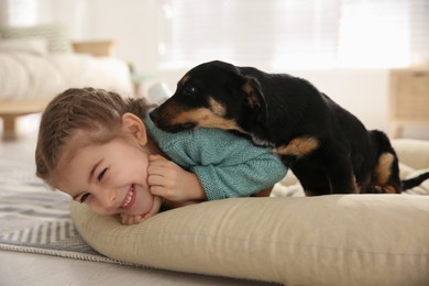 Photo of Little girl with cute puppy lying on soft pillow at home