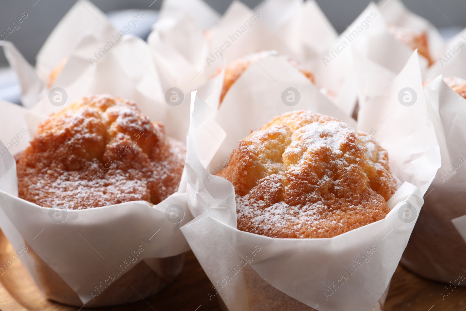 Photo of Delicious muffins with powdered sugar on wooden board, closeup