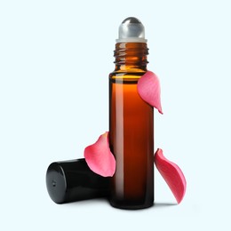 Image of Bottle of rose essential oil and flower petals on white background
