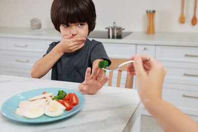 Photo of Mother feeding her son in kitchen, closeup. Little boy refusing to eat dinner