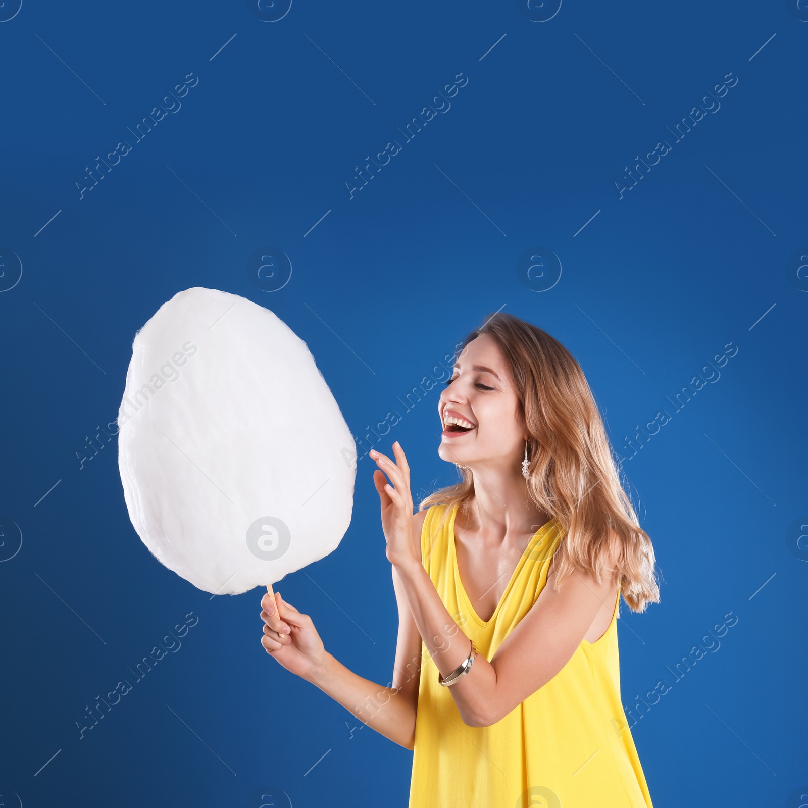 Photo of Happy young woman with cotton candy on blue background