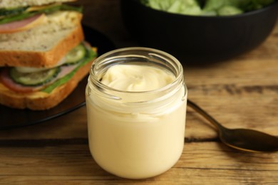 Photo of Jar of delicious mayonnaise near fresh sandwiches on wooden table