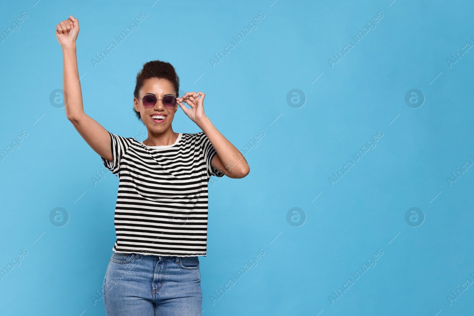 Photo of Happy young woman in stylish sunglasses dancing on light blue background. Space for text
