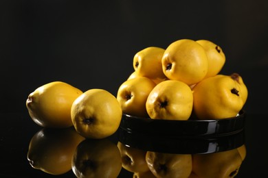 Photo of Tasty ripe quinces in bowl on black mirror surface