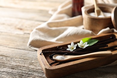 Photo of Vanilla pods, flowers, leaves and spoon with sugar on wooden table, closeup. Space for text