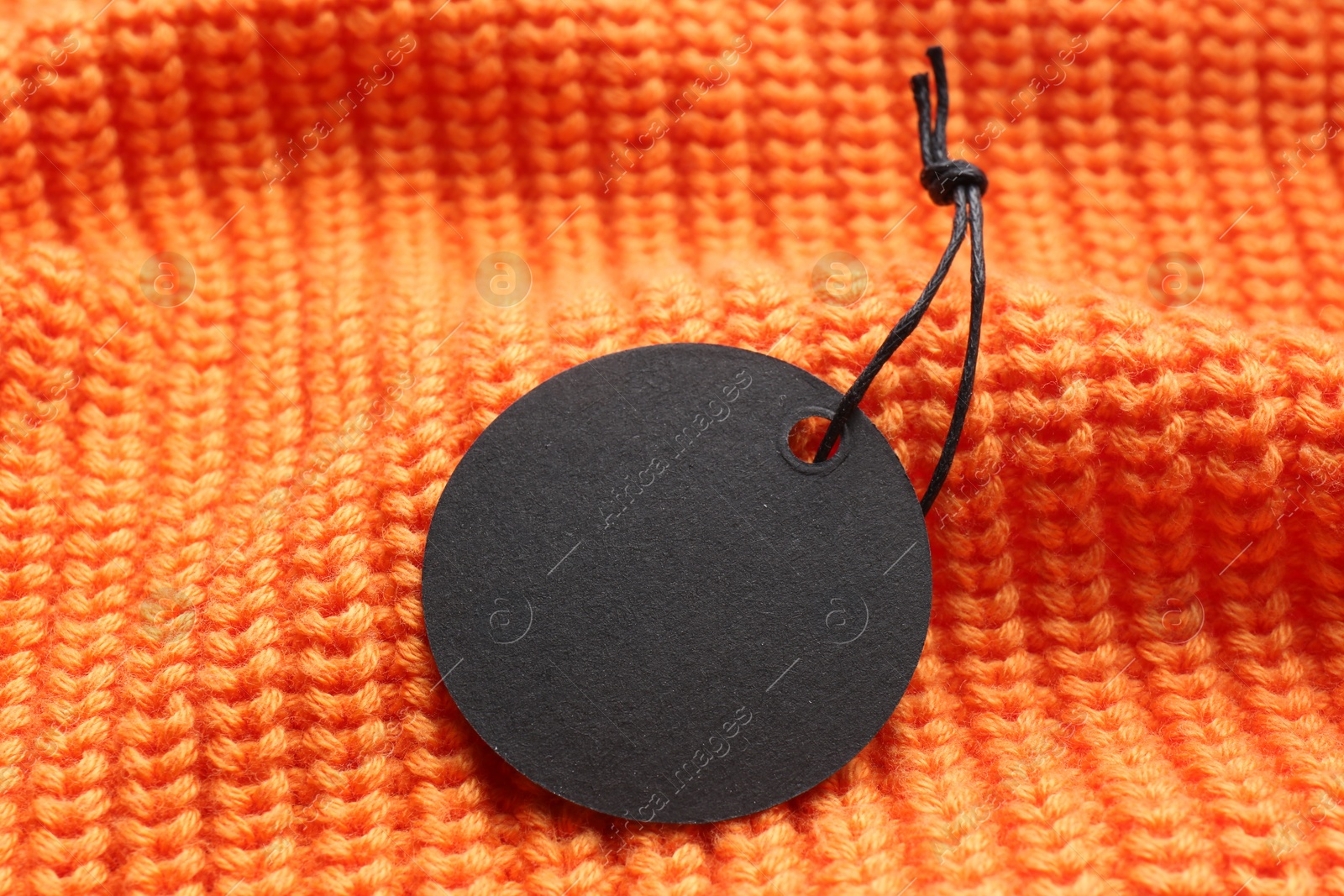 Photo of Circle shaped tag with space for text on orange knitted background, closeup