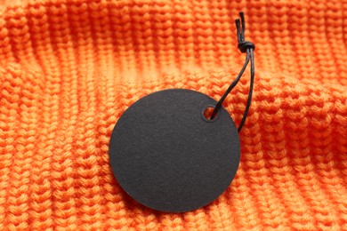 Photo of Circle shaped tag with space for text on orange knitted background, closeup
