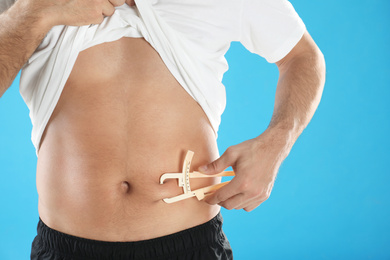 Photo of Man measuring body fat layer with caliper on light blue background, closeup. Nutritionist's tool