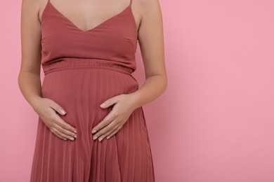 Pregnant woman in dress on pink background, closeup. Space for text