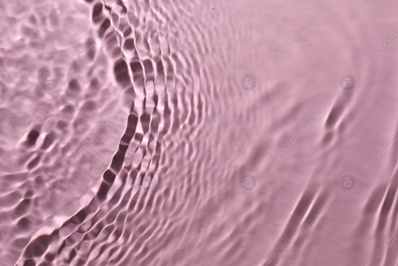 Photo of Rippled surface of clear water on pink background, top view