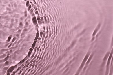 Photo of Rippled surface of clear water on pink background, top view