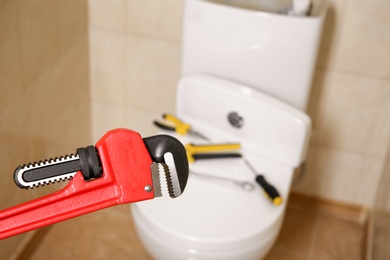 Photo of Pipe wrench near toilet indoors. Plumber's tools