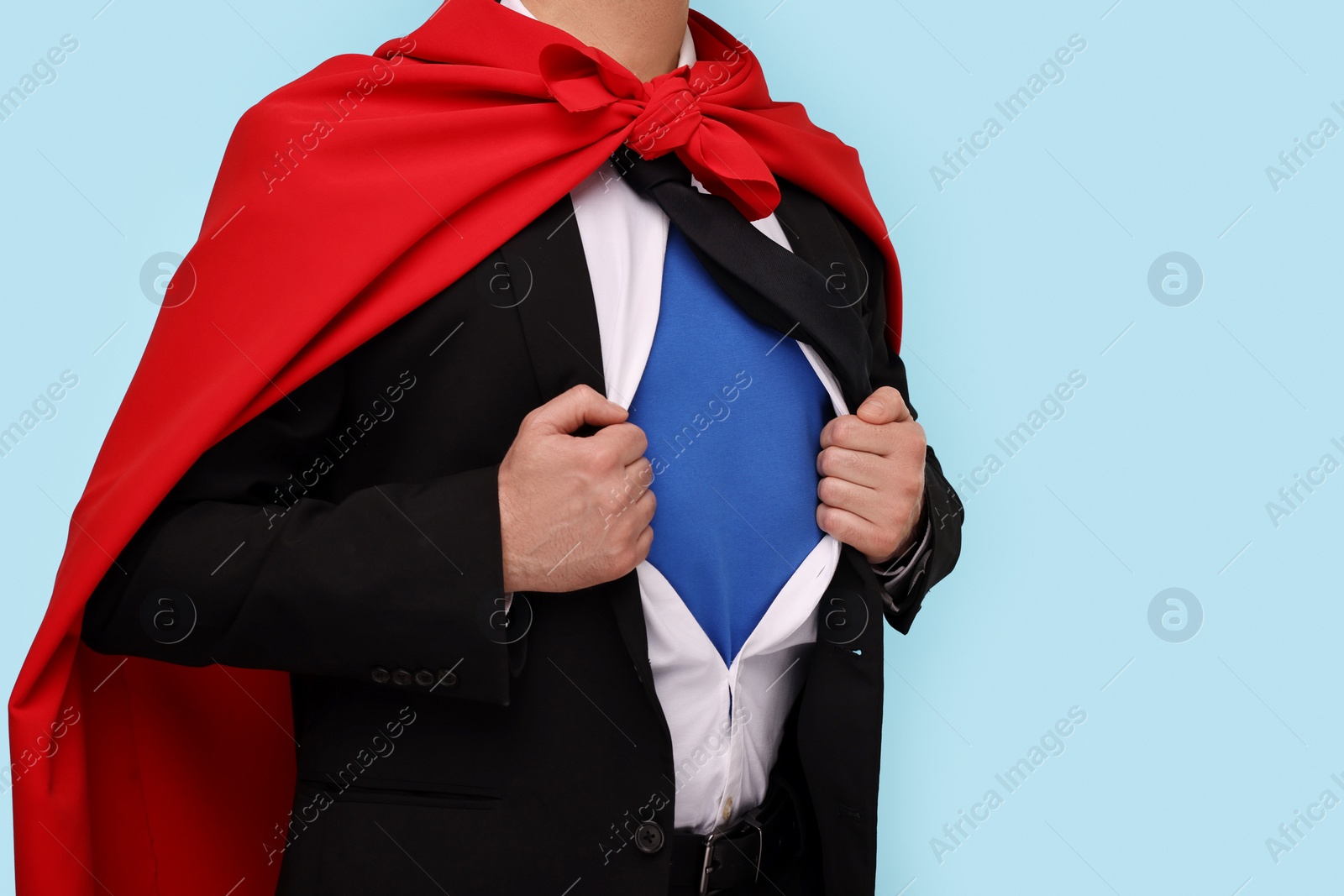 Photo of Businessman wearing superhero costume under suit on light blue background, closeup