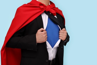 Photo of Businessman wearing superhero costume under suit on light blue background, closeup