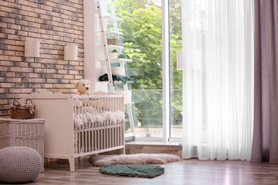 Photo of Baby room interior with crib near brick wall