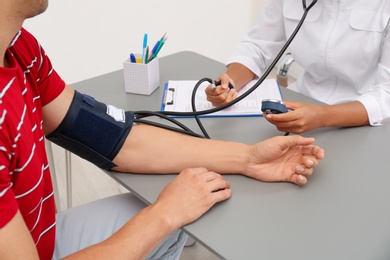 Photo of Doctor checking patient's blood pressure at table in office, closeup