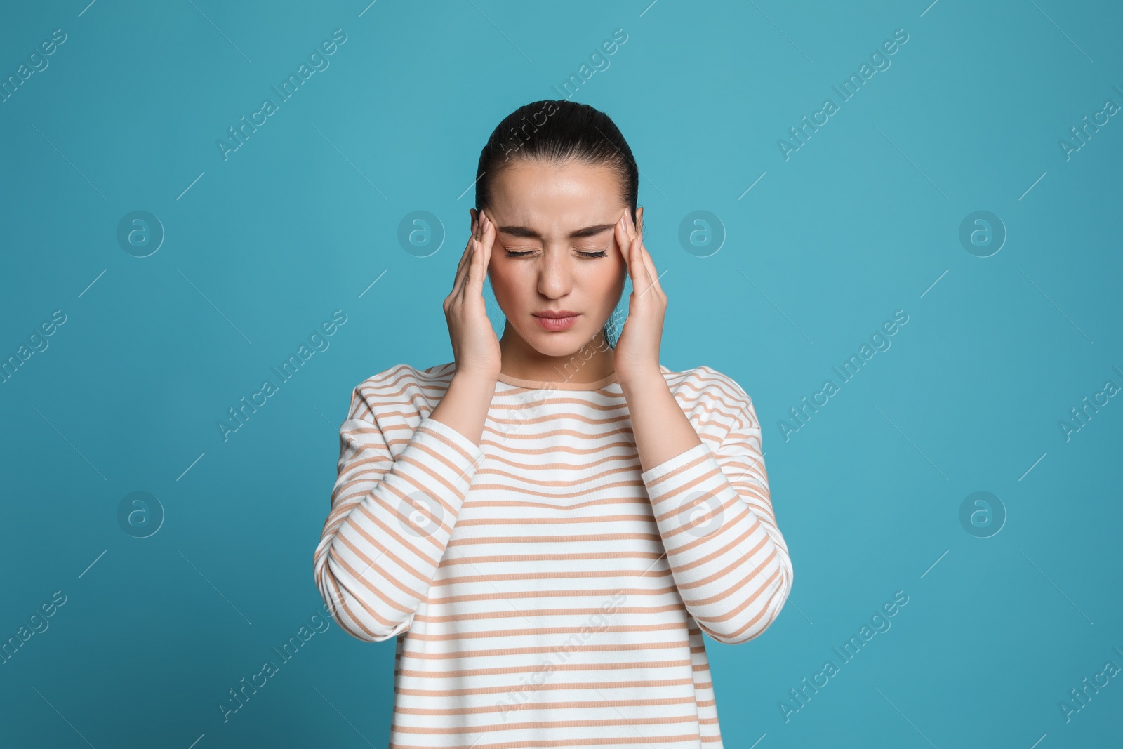 Photo of Young woman suffering from headache on light blue background