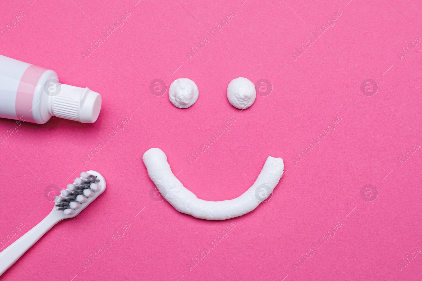 Photo of Funny face made with toothpaste, brush and tube on pink background, flat lay