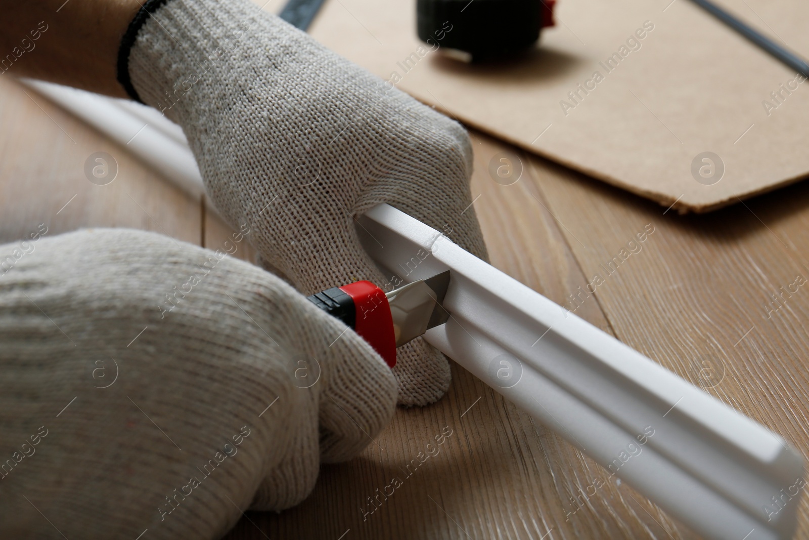 Photo of Worker cutting foam crown molding with utility knife at wooden table, closeup