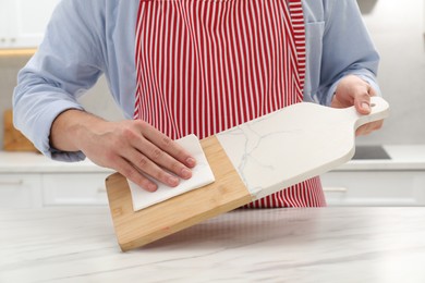 Photo of Man wiping cutting board with paper napkin at white table, closeup