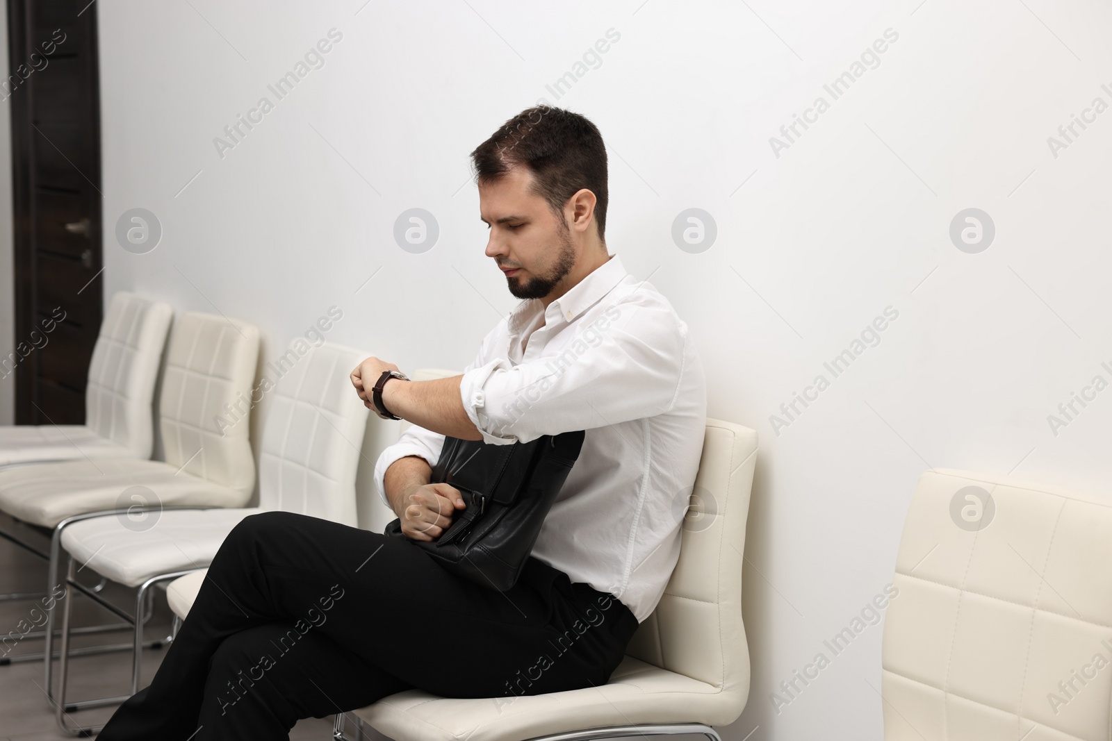 Photo of Man looking at wrist watch and waiting for job interview indoors