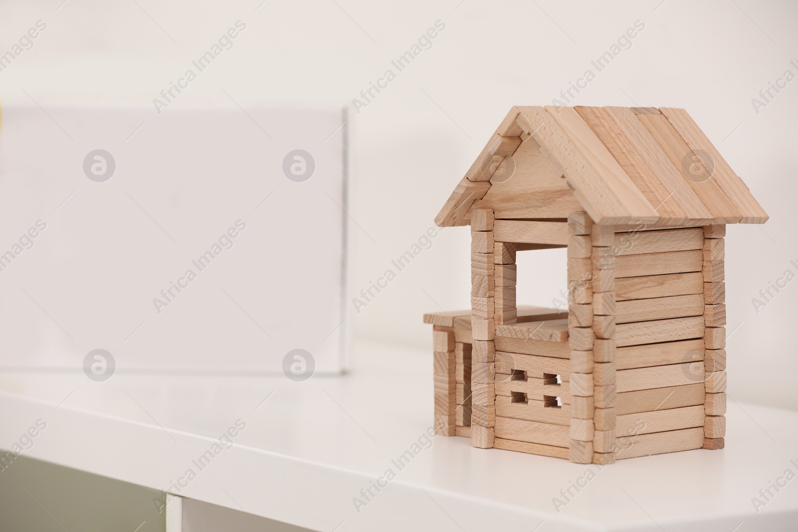 Photo of Wooden house on white shelf indoors, space for text. Educational toy for motor skills development