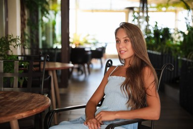 Photo of Beautiful young woman sitting on indoor terrace in cafe, space for text