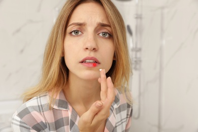 Image of Woman with herpes applying cream onto lip in bathroom